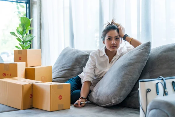 Beautiful Asian women sitting on sofa with many parcel box with small businesses sell to customer on shopping online. Concept selling and shopping online from home