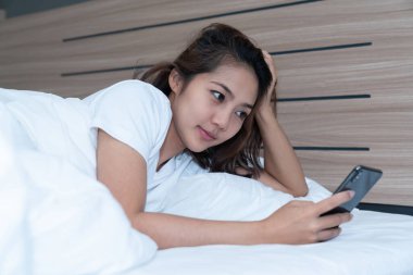 Genç Asyalı kadınlar, geceleri uyuduktan sonra yataktaki akıllı telefonlarda mesajlaşıp sosyal uygulamaları kontrol ediyorlar. Mobil bağımlılık kavramı.