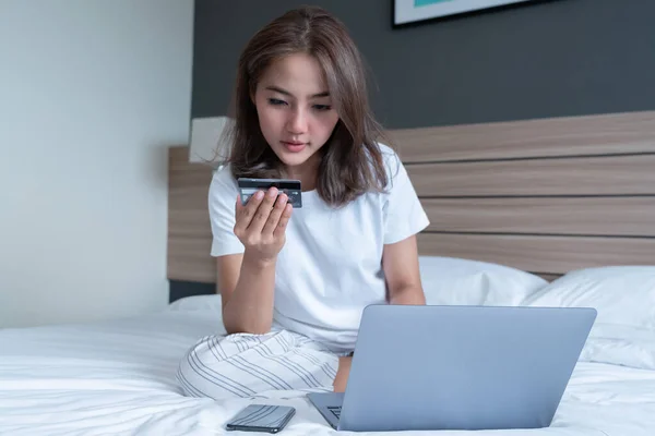 Beautiful Asian women on the bed with laptop and credit card, she shopping online, Pay utility bills, buy ticket in the morning. Morning relax time for shopping online