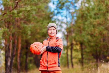 Şapkalı bir genç balkabağını açık havada tutuyor.