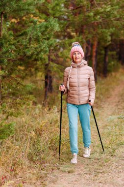60 yaşındaki spor giyimli yaşlı bir kadın sonbaharda ormanda sopalarla yürüyen İskandinavya 'da nişanlanıyor.