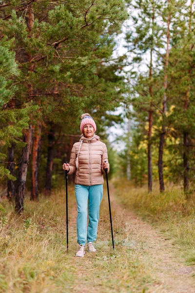 Scaninav yürüyüşü için sopaları olan spor giyimli yaşlı bir kadın.