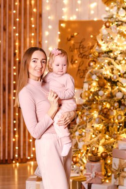 Mutlu, genç bir anne Noel ağacının yanında bir yaşında bir kız çocuğu tutuyor. Noel fotoğraf çekimi