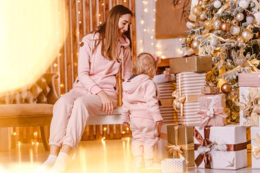 Genç, mutlu bir anne ve iki yaşındaki pembe kapüşonlu bir kız. Kapalı bir Noel ağacının yanında.