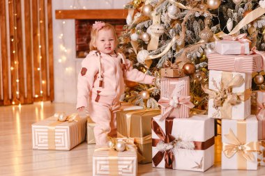 Pembe ve güzel Noel hediyeleri içinde iki yaşında bir kız çocuğu ağacın altında.