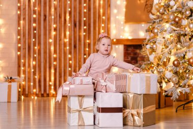 Pembe ve güzel Noel hediyeleri içinde iki yaşında bir kız çocuğu ağacın altında.