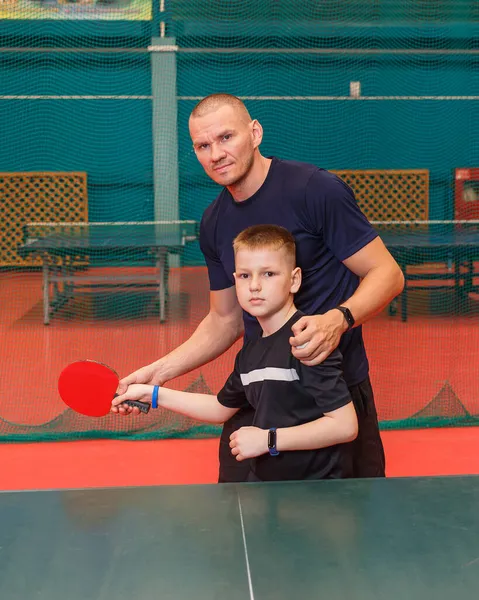 short-strimmed man trains a child to play table tennis.