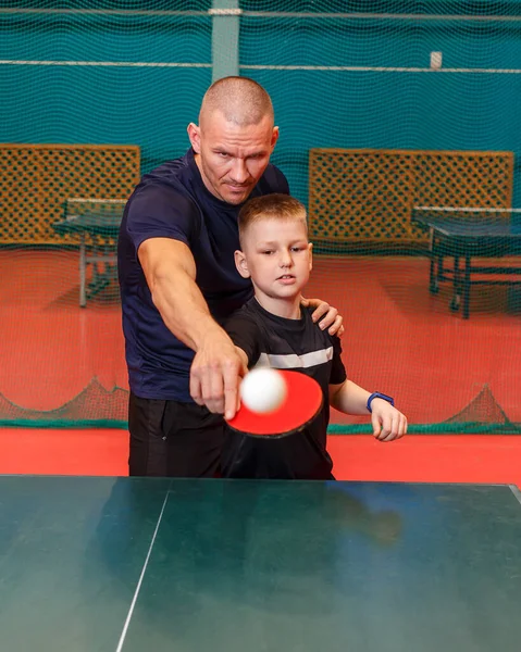 short-strimmed man trains a child to play table tennis.
