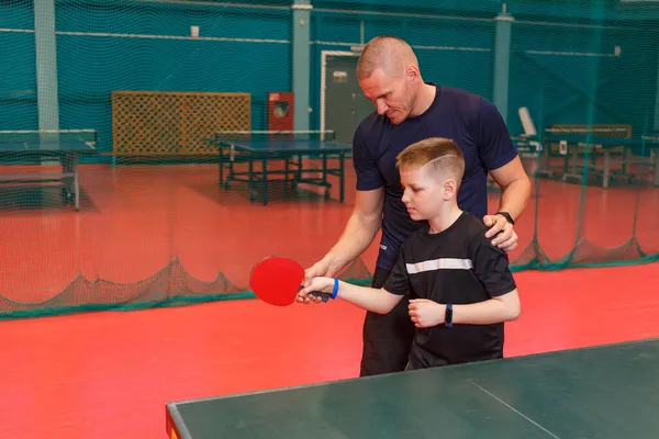 a man teaches a ten-year-old boy to play table tennis