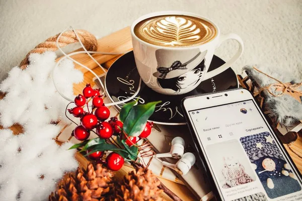 Cup of coffee and phone on a wood tray with christmas decorations and cones