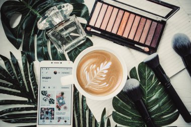 Yazın bir fincan kahve, göz farı paleti ve beyaz ahşap arka planda telefon.