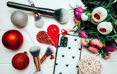 Telefon ve makyaj fırçaları ahşap arka planda Noel süslemeleri ve çiçeklerle