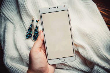 Küpeli yumuşak süveterin arka planında kadın eli telefon.