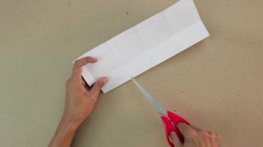 El işi yapmak. Bir parça beyaz karton kesiyorum. Makas kullanılır. Kahverengi eller. İspanyol tenli. Eğitici aktivite. Origami, el sanatları ve diğer sanatlar.