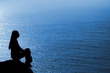 Sitting woman silhouette against deep blue seascape clipart