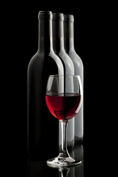 Elegante bicchiere di vino rosso e bottiglie di vino in sfondo nero — Foto Stock