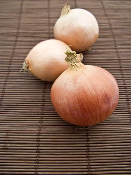 Tres cebollas sobre una estera de paja —  Fotos de Stock