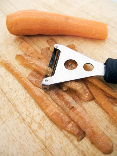 Carota e pelapatate su tavola di legno — Foto Stock