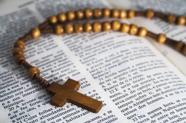 Open Bible with rosaries-beads crucifix on a straw table — Stock Photo, Image
