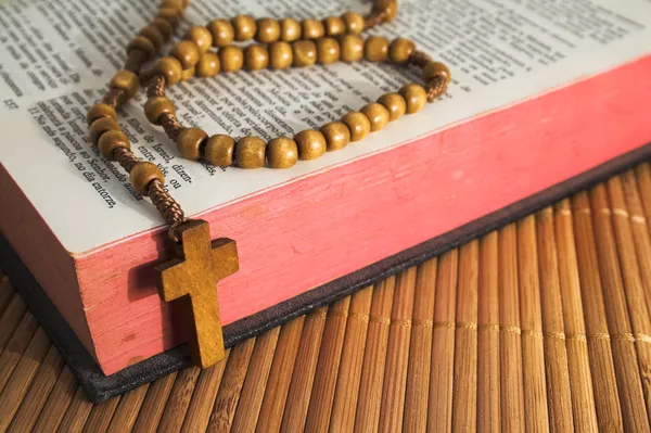 Open Bible with rosaries-beads crucifix on a straw table — Stockfoto