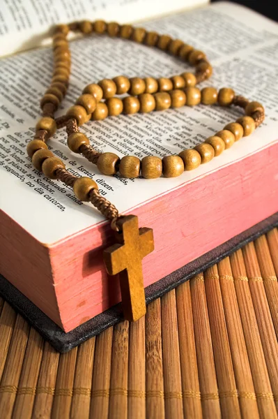 Open Bible with rosaries-beads crucifix on a straw table — Stockfoto