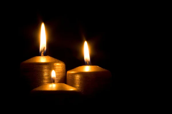 Tres velas doradas ardiendo en la oscuridad — Foto de Stock