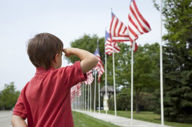 Boy salutes flags at Memorial Day display in a small town clipart