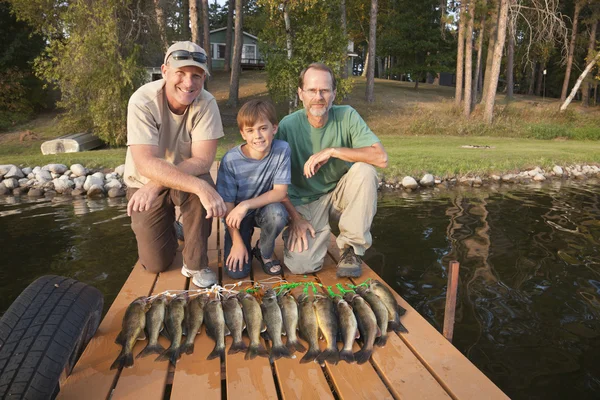 Två män och en pojke som poserar med fångst av fisk — Stockfoto