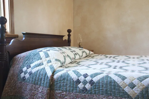 Old fashioned bed with quilt and oil lamp — Stock Photo, Image