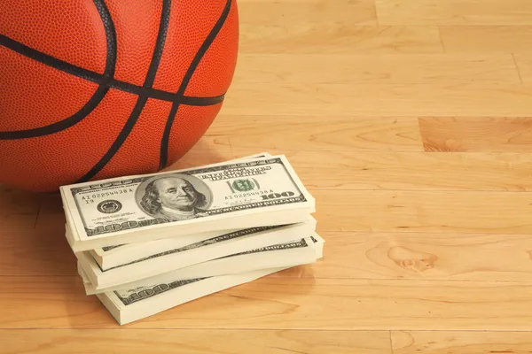 Basketball and one hundred dollar bills on wooden court floor — Stock Photo, Image