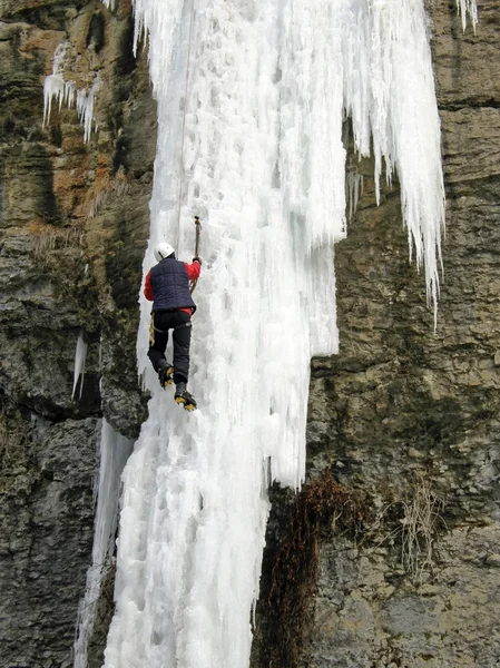Um escalador de gelo subindo uma cachoeira congelada . — Fotografia de Stock