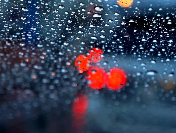Defokussierter Verkehr, betrachtet durch eine Autoscheibe, die mit Regen bedeckt ist, Fokus auf Regentropfen — Stockfoto