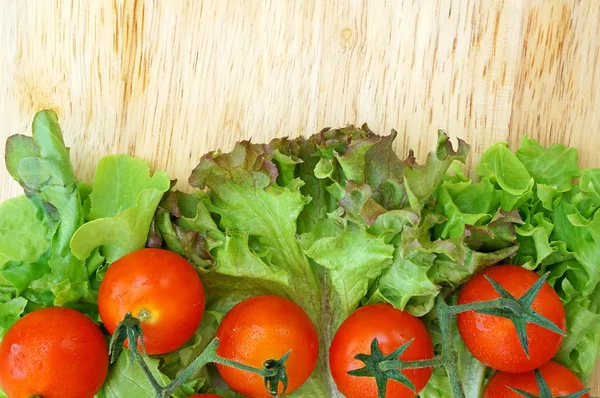 Tomates e alface sobre fundo de madeira — Fotografia de Stock