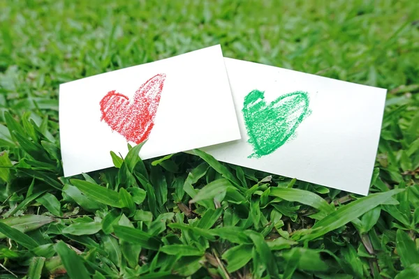 Desenho de papel forma coração vermelho na grama verde — Fotografia de Stock