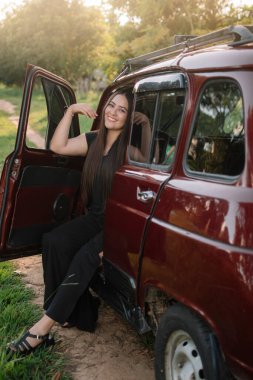 Doğanın ortasında bir arabanın üzerinde rahat bir kız ve güzel bir manzara.