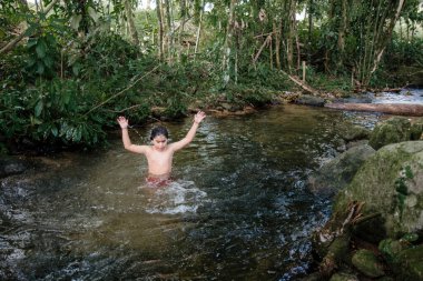 Çocuk suda oynuyor ve doğayla iç içe eğleniyor.