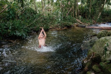Çocuk suda oynuyor ve doğayla iç içe eğleniyor.