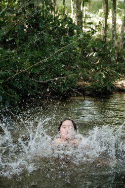 Çocuk suda oynuyor ve doğayla iç içe eğleniyor.