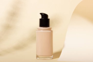 Arka planda gölgeli cam bir şişenin içindeki temel. Bej arkaplanda kopya alanı olan yüz düzeltici. Kopyalama alanı olan paketleme modeli