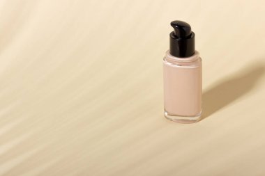 Arka planda gölgeli cam bir şişenin içindeki temel. Bej arkaplanda kopya alanı olan yüz düzeltici. Kopyalama alanı olan paketleme modeli