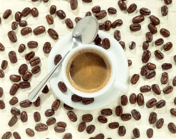 Kopje schuimend koffie omringd door koffie bonen — Stockfoto