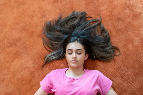 オレンジの床に目を閉じて横に長い暗い髪を持つ平和的な女性のティーンエイジャーの上から — ストック写真
