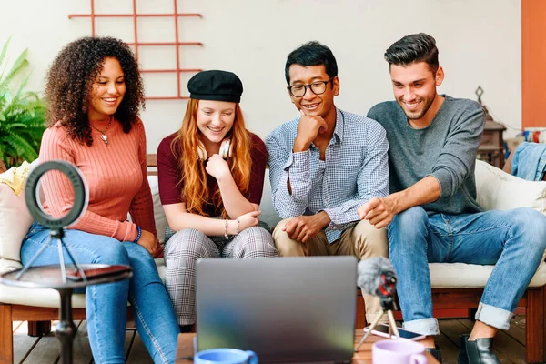 Neşeli çoklu etnik arkadaşlar rahat koltukta oturup dizüstü bilgisayarda film izliyorlar.