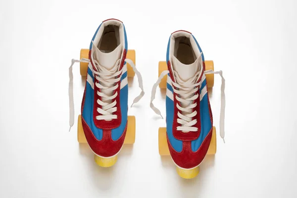 黄色の車輪と白い表面に配置された靴ひもを持つ青と赤のブーツと古い様式のクワッドローラースケートのペアのトップビュー — ストック写真