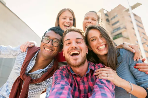 Low angle portrait of a cheerful interracial group of five friends smiling while taking a selfie picture outdoors in the city