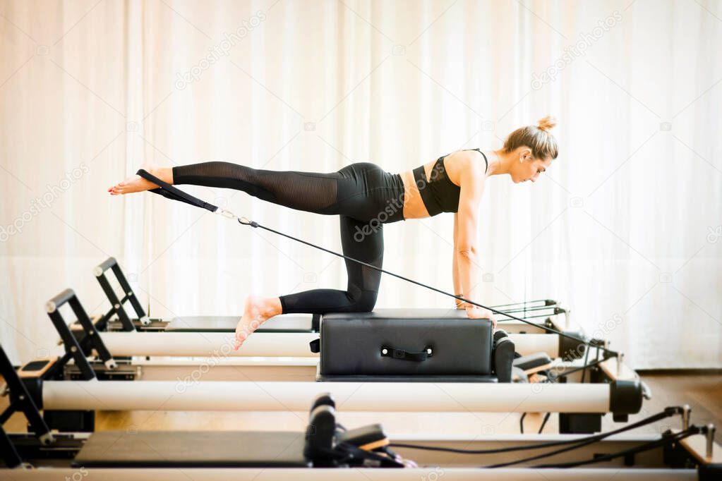 Fit woman performing a pilates diagonal stabilisation exercise using a strap on a reformer bed in a gym in a fitness concept