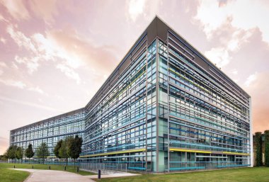 Gün batımında bulutlu gökyüzünün altında saydam cam duvarları olan çok katlı ticaret binasının köşesinde.