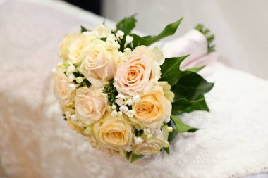 Masanın üzerine beyaz dantelli masa örtüsü serpiştirilmiş taze aromatik güllerle gelin buketinin yukarısından.