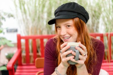 Bahçedeki bankta yeşil bitkilerle otururken şapkalı mutlu bir kadın gözlerini kaçırıyor.