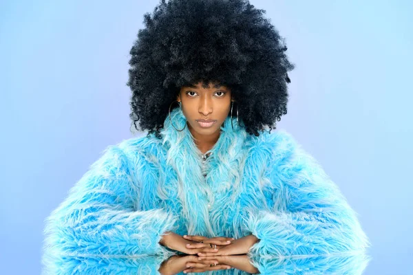ドミニカの女性モデルとともにアフリカの髪型で毛皮の青いコート見ますカメラでミラーテーブル上の青の背景 — ストック写真
